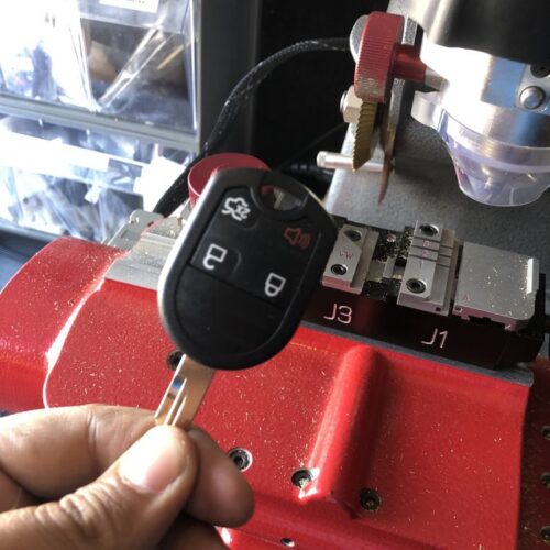 A freshly cut Ford remote-head key held beside the key cutting machine in the van.
