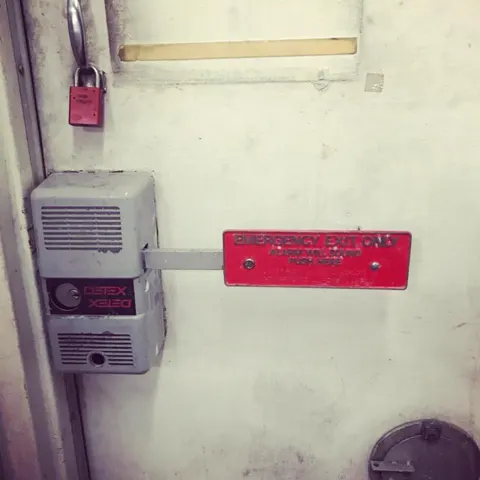 A commercial emergency exit device with red push bar and alarm housing
