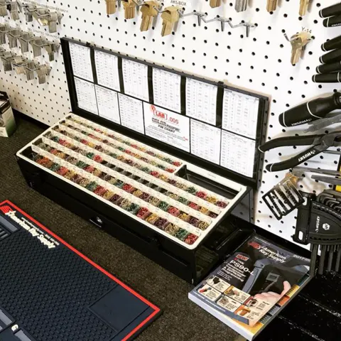 A case of organised key blanks under a pegboard of key machines