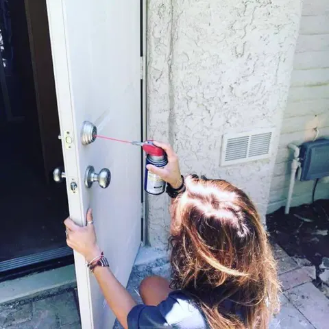 A technician spraying lubricant into a residential front-door lock