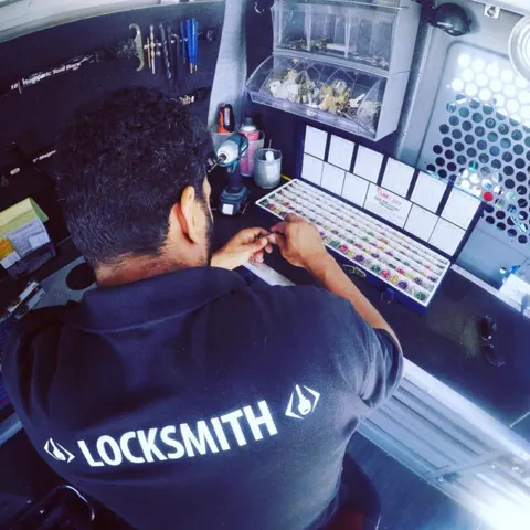 A technician in a LOCKSMITH shirt at the key bench in the van